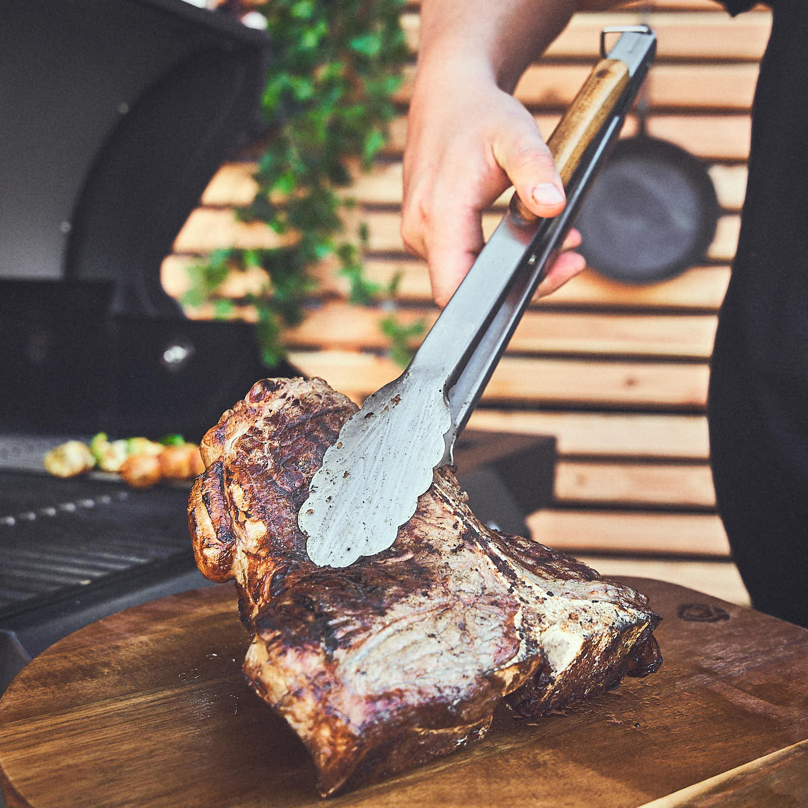 Fleisch mit der Grillzange auf Schneidebrett ablegen Fleisch mit der Grillzange auf Schneidebrett ablegen