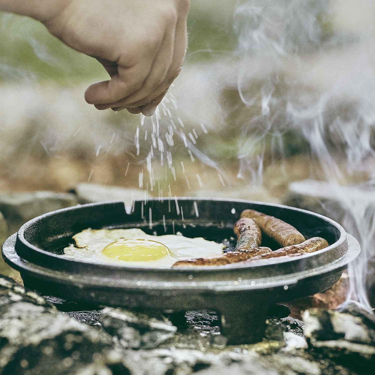 Über Lagerfeuer wird Essen im Dutch Oven Deckel zubereitet und gewürzt Über Lagerfeuer wird Essen im Dutch Oven Deckel zubereitet und gewürzt
