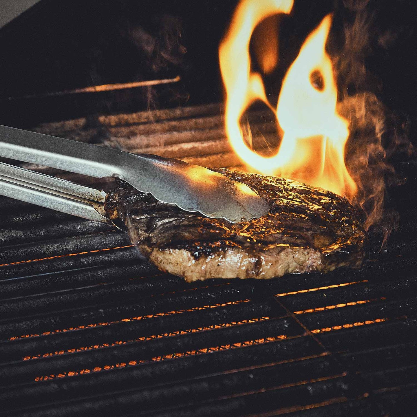 Akazienholz-Grillbesteck-Set Fleisch wird mit Grillzange auf dem Rost bewegt Akazienholz-Grillbesteck-Set Fleisch wird mit Grillzange auf dem Rost bewegt