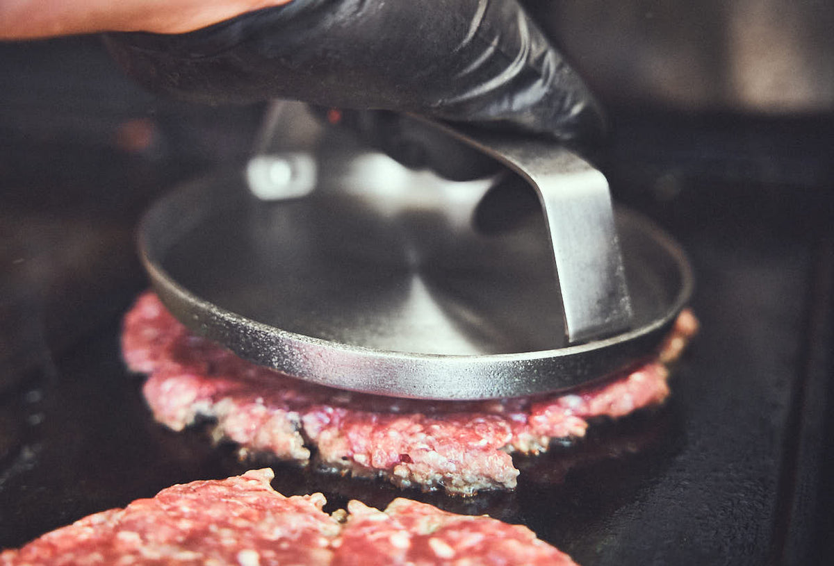 Grillszene Patties werden mit Burger Smasher platt gedrückt Grillszene Patties werden mit Burger Smasher platt gedrückt