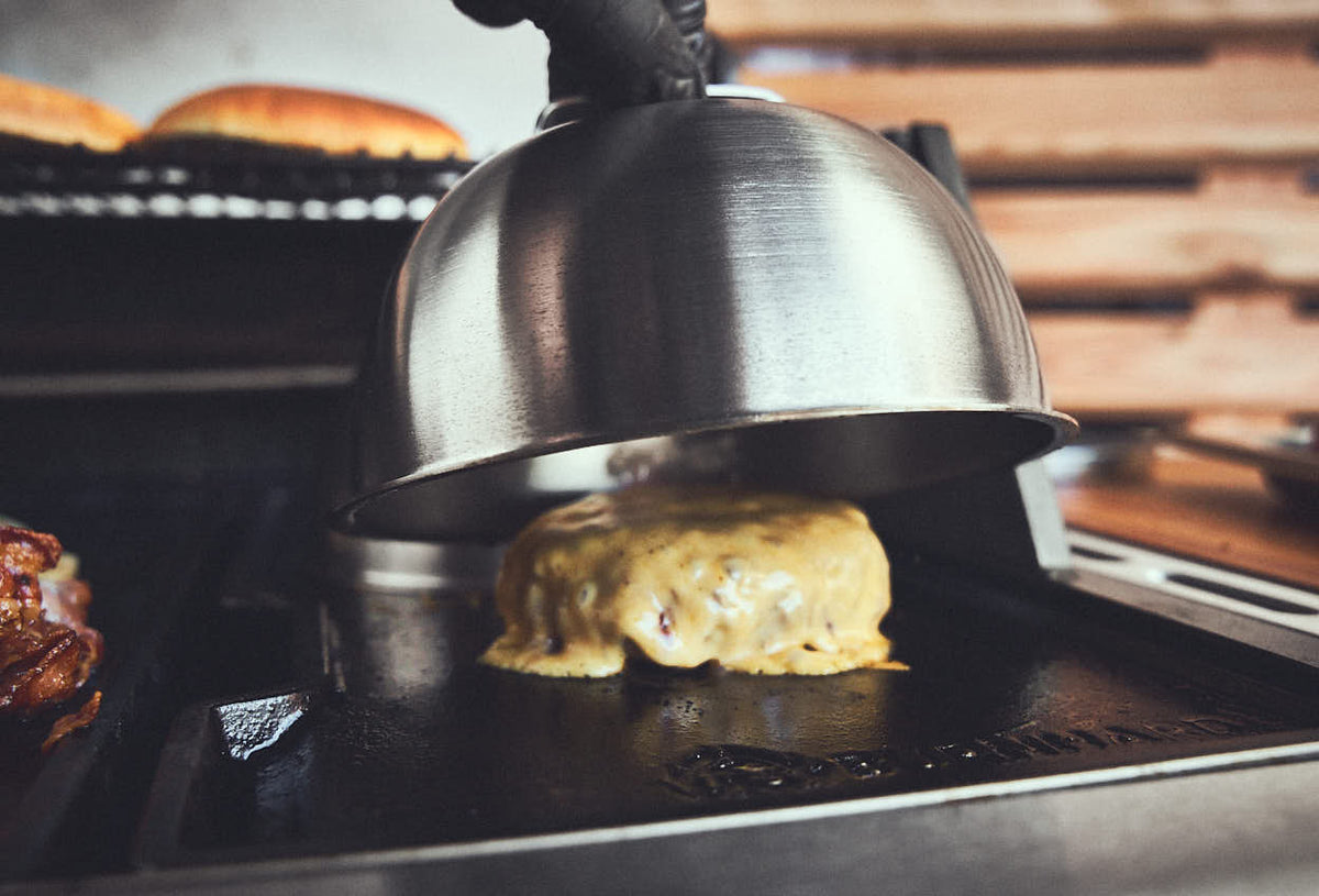 Grillszene Patty mit schmelzender Käsescheibe unter Burgerglocke Grillszene Patty mit schmelzender Käsescheibe unter Burgerglocke