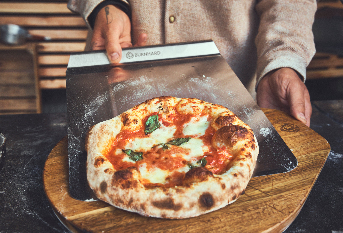 Fertig gebackene Pizza wird mithilfe der Schaufel auf dem Pizzabrett abgelegt Fertig gebackene Pizza wird mithilfe der Schaufel auf dem Pizzabrett abgelegt
