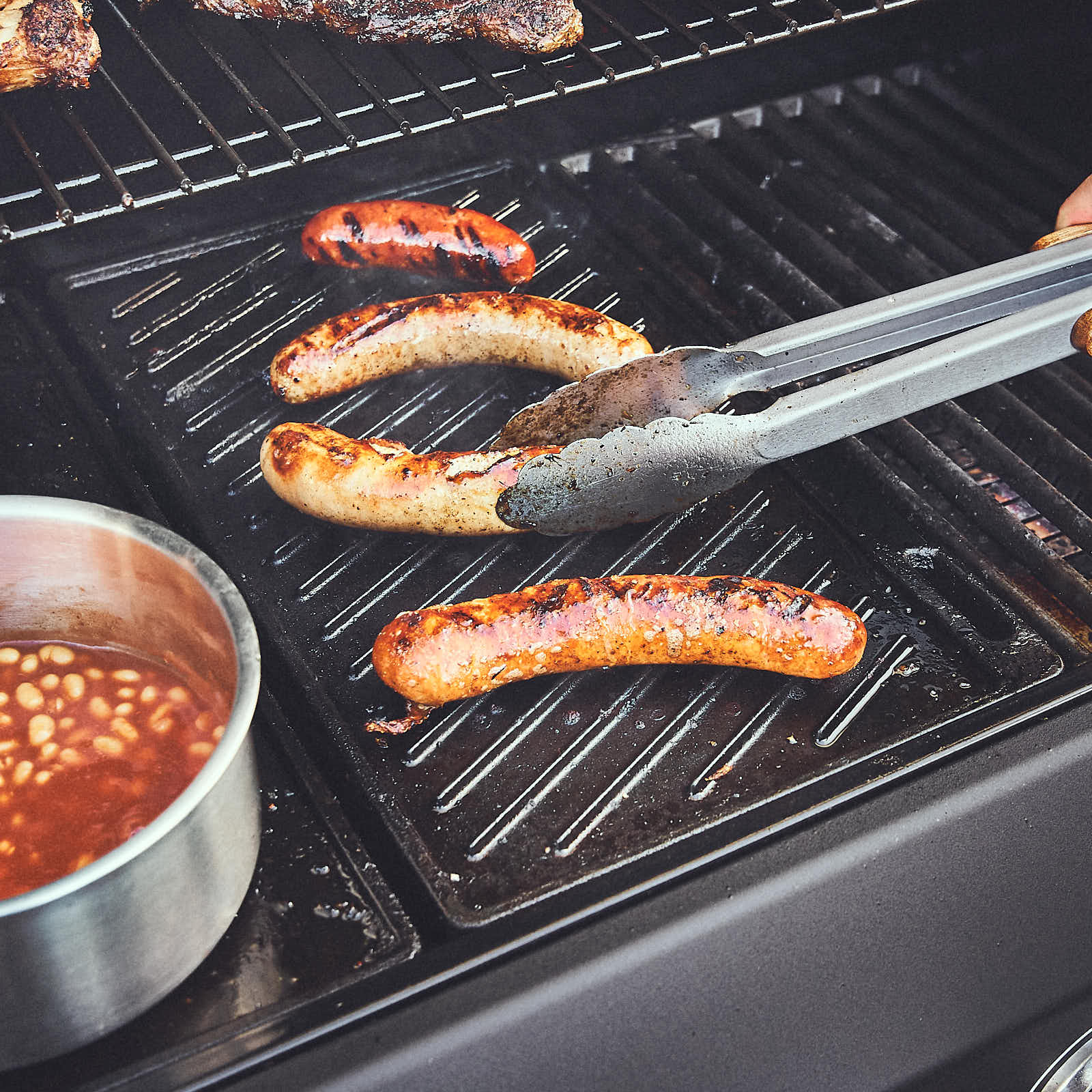 Grillszene Bratwürste auf der geriffelten Seite der Wendeplatte zubereiten Grillszene Bratwürste auf der geriffelten Seite der Wendeplatte zubereiten