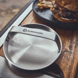 Image 35780214653243 Grillszene Smasher lehnt an Schneidebrett im Hintergrund fertiger Burger auf Teller