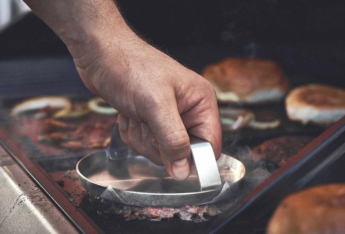 Grillszene Patty auf dem Grill wird mit Burger Smasher platt gedrückt Grillszene Patty auf dem Grill wird mit Burger Smasher platt gedrückt