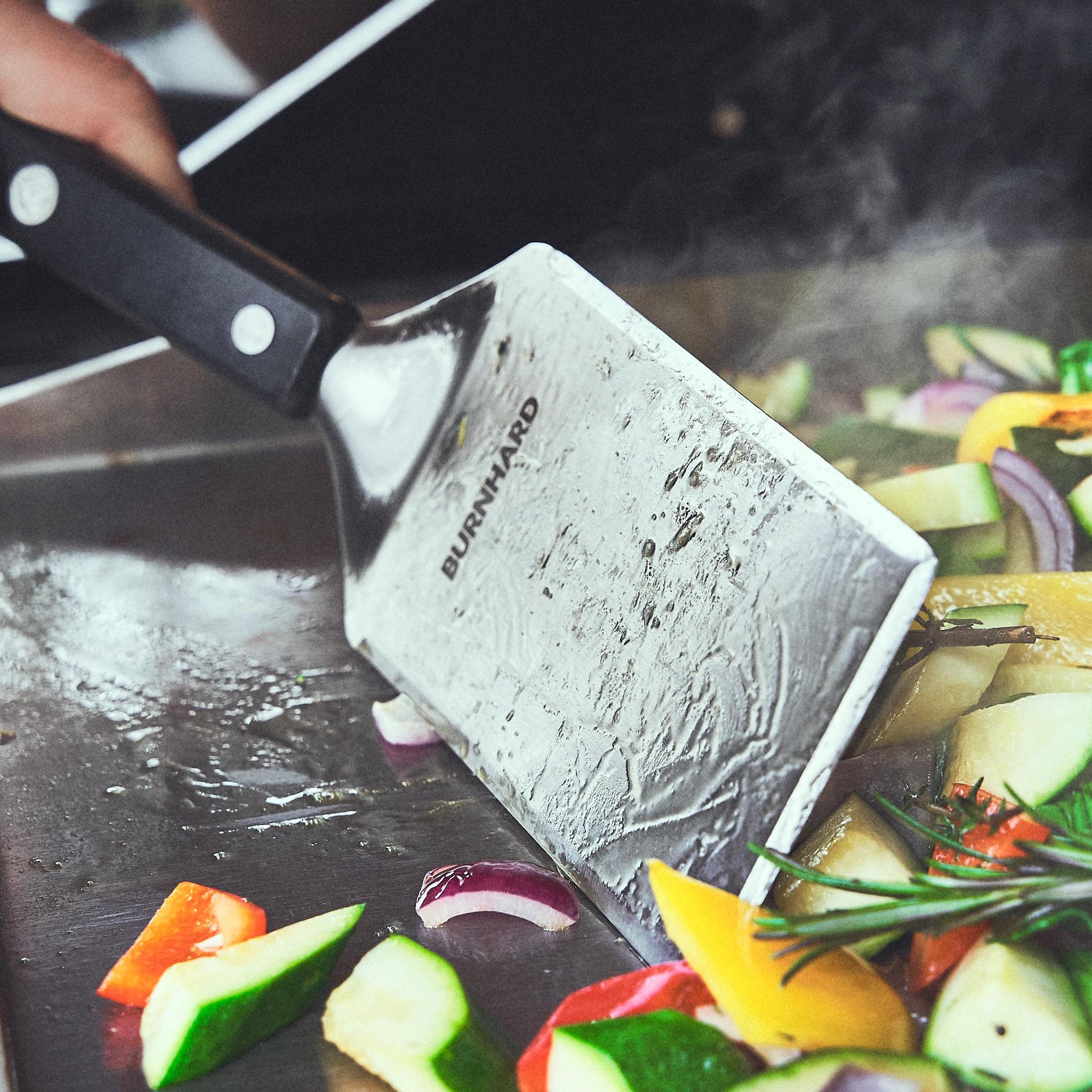 Grillgemüse wird mit dem Grillspachtel auf der Plancha bewegt Grillgemüse wird mit dem Grillspachtel auf der Plancha bewegt