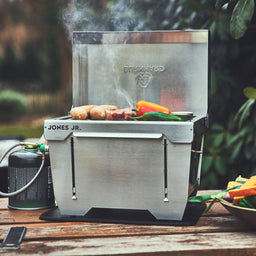 Image 64039426687349 Burnhard JONES Jr. 1-Brenner Klappgrill mit Würstchen und Grillgemüse auf einem Picknick Tisch
