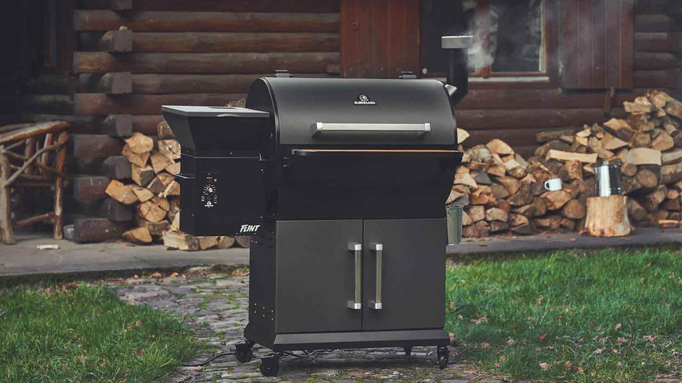 Pelletsmoker mit rauchendem Schornstein draußen vor Holzhütte Pelletsmoker mit rauchendem Schornstein draußen vor Holzhütte