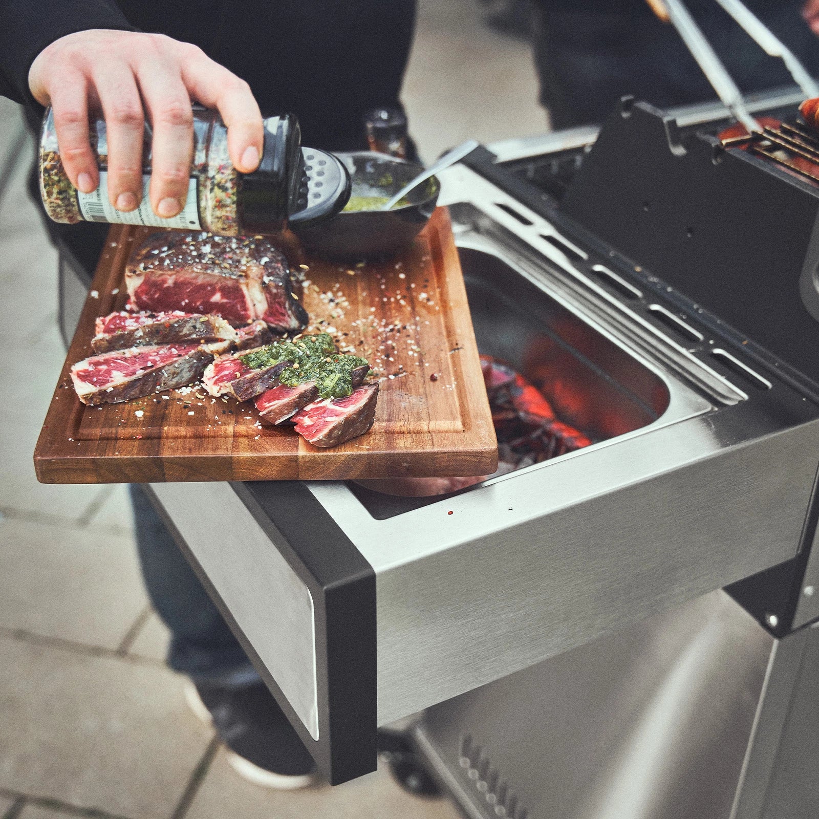 Grillszene in der Fleisch auf dem Schneidebrett am Seitentisch gewürzt wird Grillszene in der Fleisch auf dem Schneidebrett am Seitentisch gewürzt wird