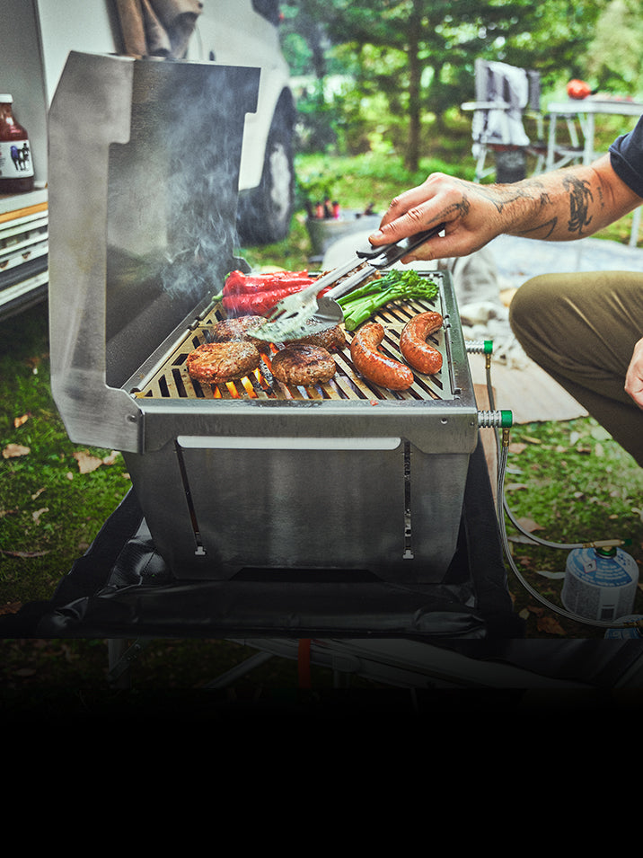 JONES Campinggrill 2-Brenner vor Camper-Van belegt mit Würstchen, Frikadellen und Gemüse