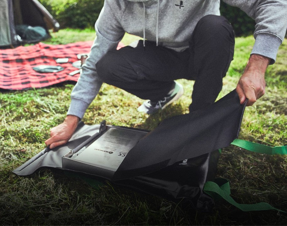 Campinggrill JONES wird auf einer Wiese zusammengeklappt aus seiner passenden Tasche ausgepackt