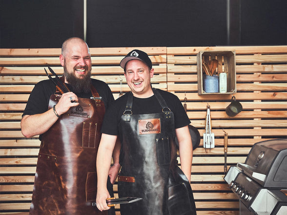 Image 35823118156091 BURNHARD Team-Mitglieder lachend mit Grillzangen in den Händen am Grill stehend