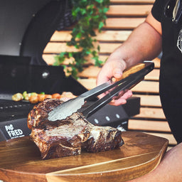 Fleisch mit der Grillzange auf Schneidebrett ablegen