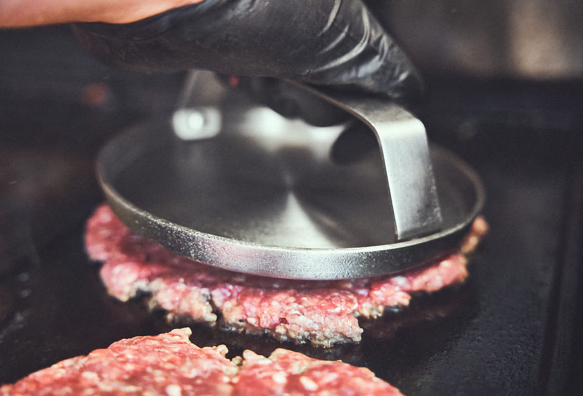 Grillszene Patties werden mit Burger Smasher platt gedrückt
