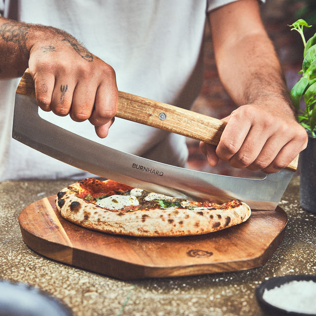 Tischszene Pizza wird mit Pizza-Wiegemesser zerteilt