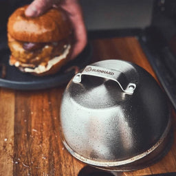 Grillszene Burgerglocken liegen nach der Nutzung auf Schneidebrett im Hintergrund wird fertiger Burger angehoben