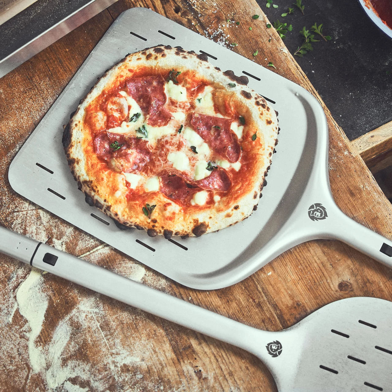 Draufsicht Tischszene Pizzaschieber und Pizzawender mit fertig gebackener Pizza auf bemehltem Tisch