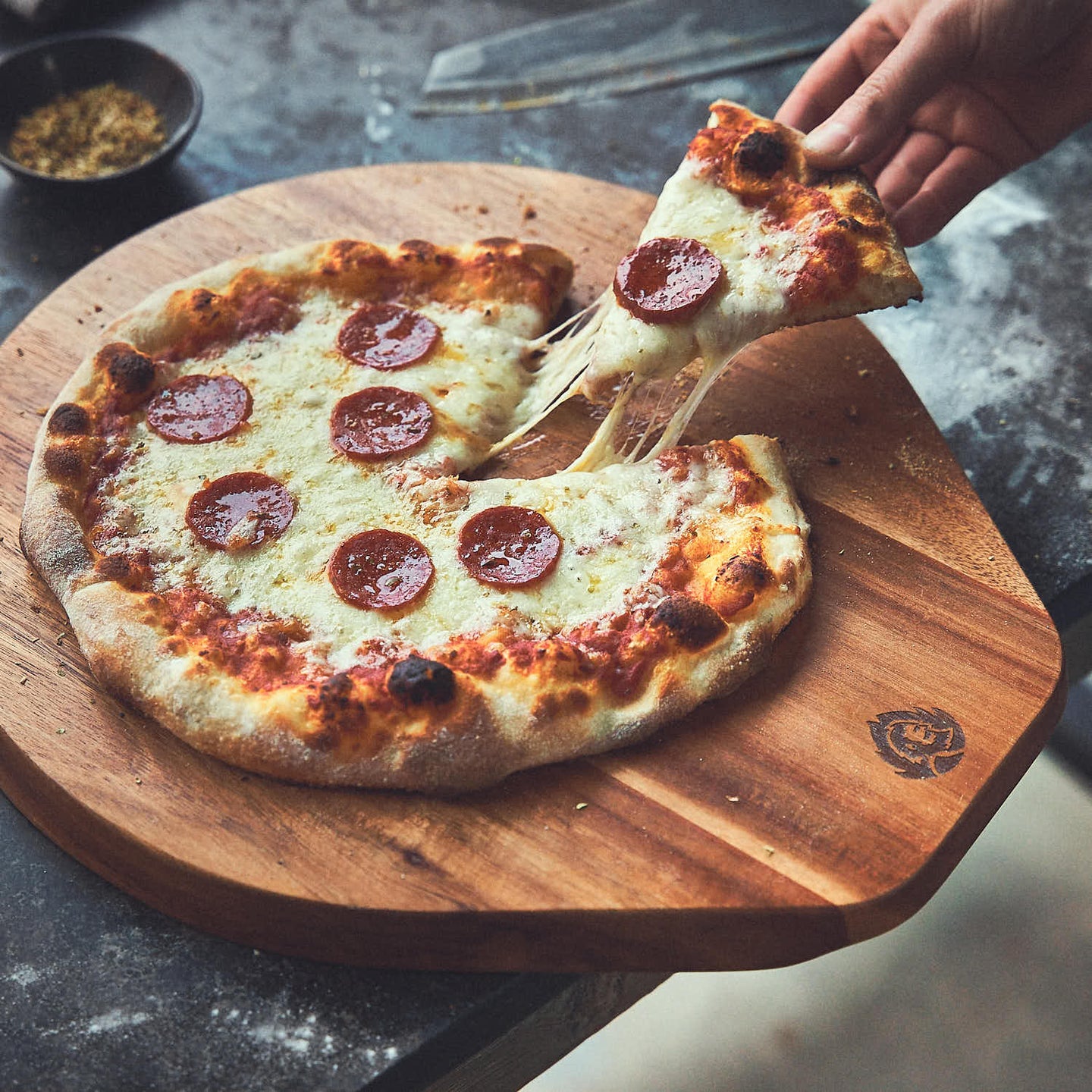 Tischszene Pizzastück mit Salami und geschmolzenem Käse wird von Pizzabrett genommen