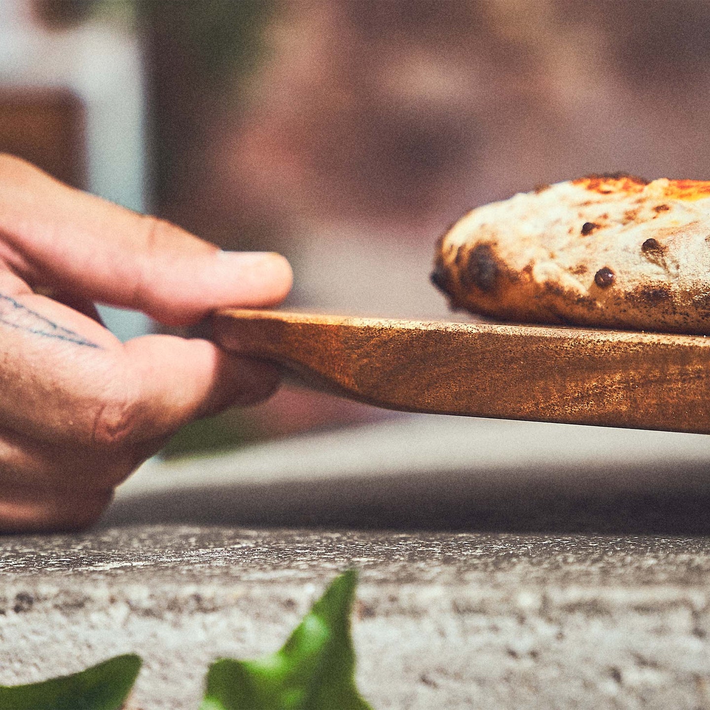 Tischszene Pizzabrett mit gebackener Pizza wird angehoben