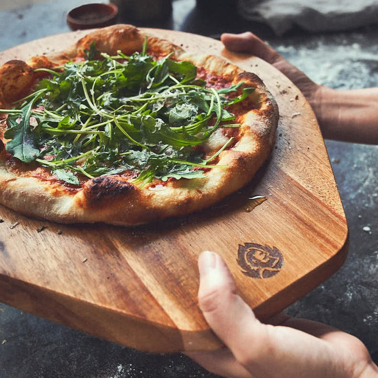 Tischszene Pizzabrett mit fertiger Pizza wird gehalten