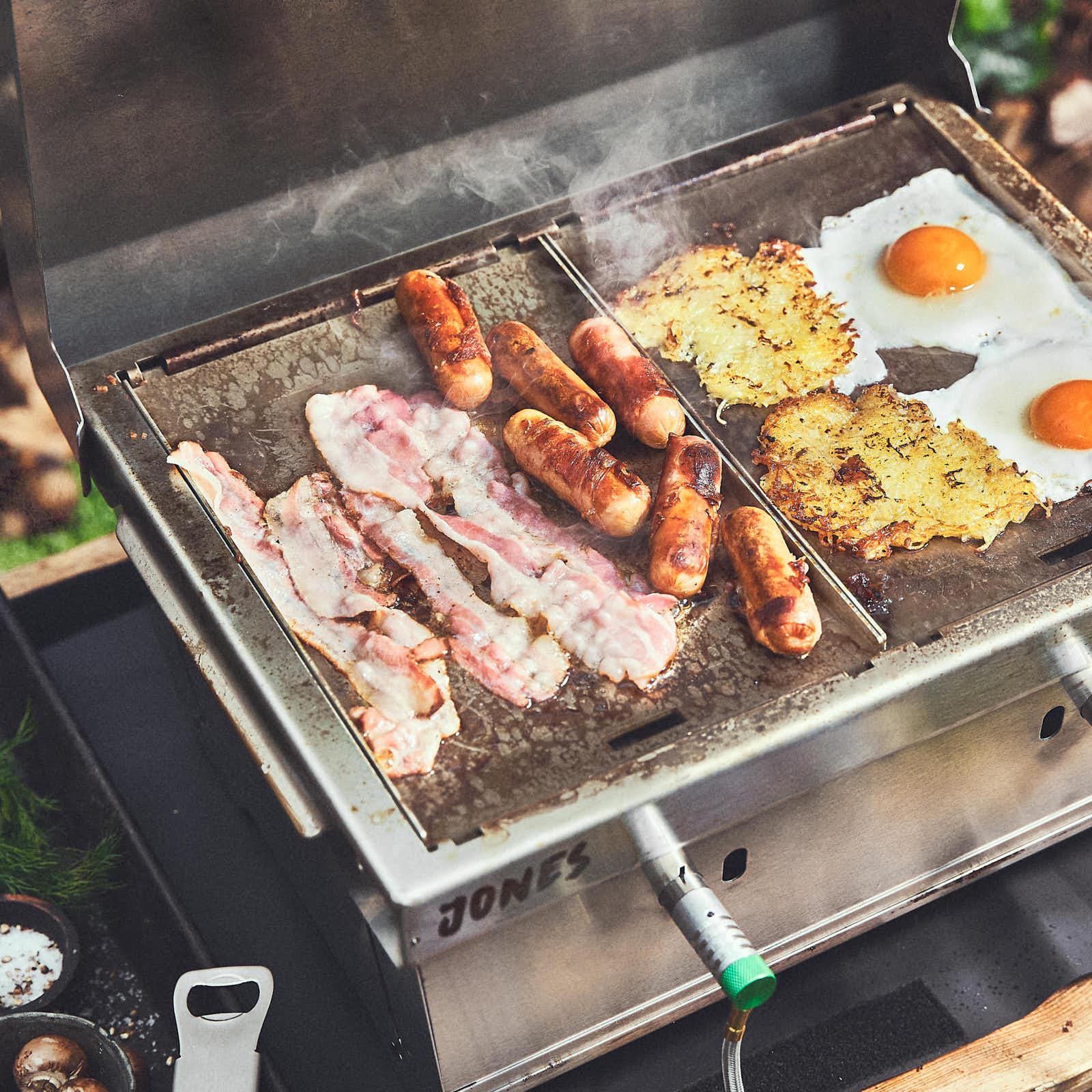 Grillszene Speck, Würstche und Spiegeleier werden auf zwei Planchas im JONES gegrillt