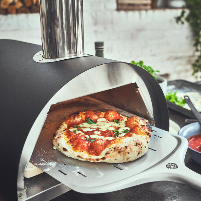 Fertig gebackene Pizza auf Pizzaschieber aus dem Ofen entnehmen