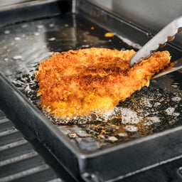 Schnitzel wird ausgebacken auf der Bratseite mit hohem Rand der Gusseisen Grillplatte 2-in-1 für modularen Gasgrill GRANT 