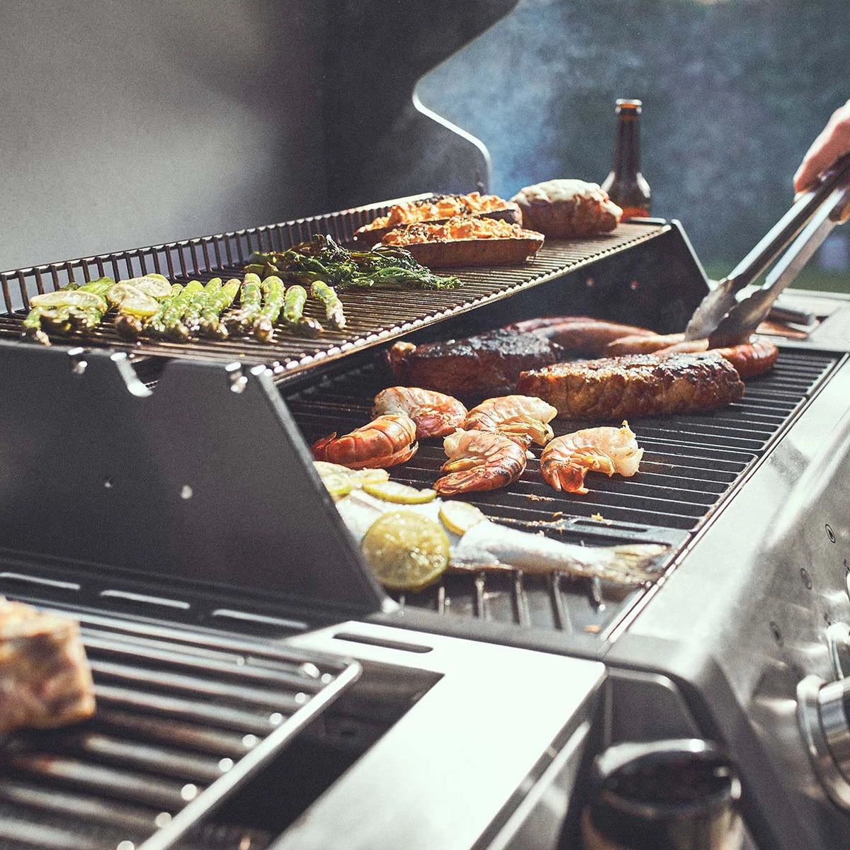 Grillszene Premium-Gasgrill 4-Brenner Big EARL mit Fleisch und Gemüse auf dem Grillrost und mittig wird ein Steak gewendet