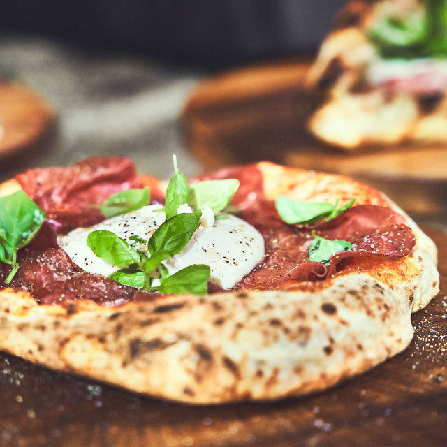 Perfekt gebackene neapolitanische Pizza mit luftigem Rand, belegt mit Burrata, Salami und Basilikum